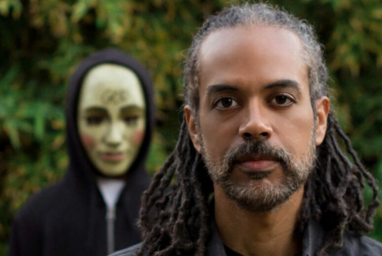 Mark H. Harris' Poortrait im Vordergrund zu sehen, im Hintergrund steht eine Figur mit unheimlicher Maske.