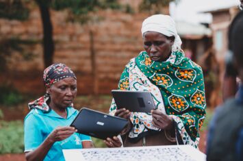 zwei Frauen schauen auf ein Tablet einen digitalen Holzstab an