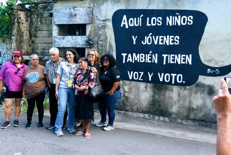 Eine Gruppe von Delegierten Caño Martin Peña CLT vor einem Wandbild mit der Aufschrift: »Hier haben auch Kinder und Jugendliche eine Stimme und ein Wahlrecht«