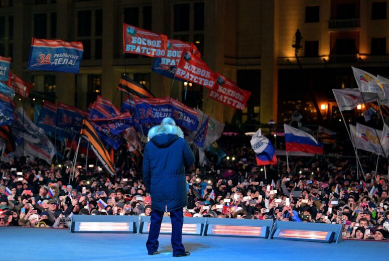 Der russische Präsident Wladimir Putin steht auf einer Bühne, Anhänger*innen schwenken Russland-Fahnen