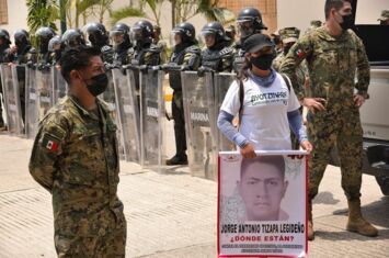 eine Studierende protestiert, umgeben von schwer geschützter Polizei und Militärs