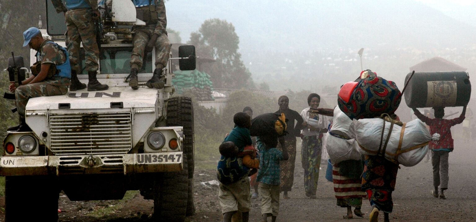 DR Kongo: Vertriebene Familien fliehen zu Fuß mit großem Gepäck. Links sitzen UN-Soldaten der MONUSCO-Mission auf einem Wagen.