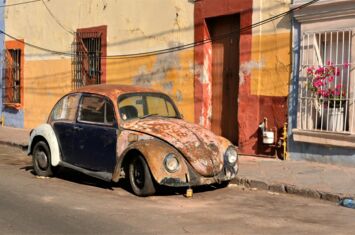 Verrostster Käfer steht vor buntem Haus in Mexiko