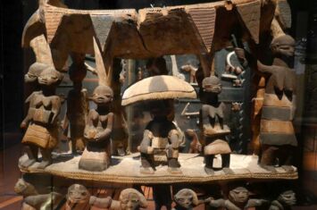 Aus Holz geschnitzte Miniaturfiguren - Königssitz mit mit Figuren der Yoruba-Kultur, ausgestellt in einer Vitrine
