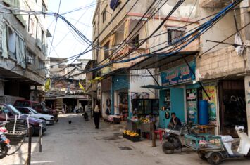 Verkabelung der Häuser sichtbar. Kleine Shops, Roller und Autos. Eine Straße in der palästinensischen Siedlung Burj al-Barajneh südlich von Beirut