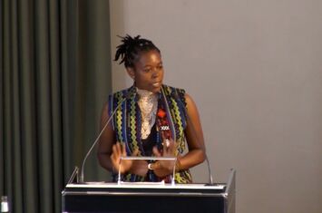 Assunta Muthoni - Speaker* am Pult in der Aula der Uni Freiburg beim SDG Hochschultag