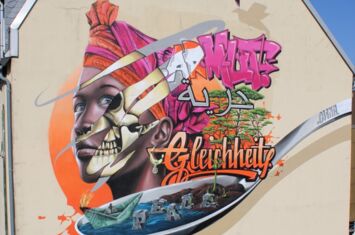 Ein Graffiti an einer Hauswand, das eine junge afrikanische Frau darstellt, sowie die entwicklungspolitischen Schlagwörter "Armut", Gleichheit" und "Peace".