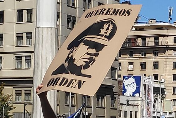 Es stehen Menschen auf der Straße und strecken ihre Arme in die Luft. Ein Plakat mit dem Foto Pinochets wird hochgehalten.