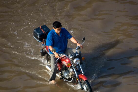 Mann fährt Motorrad durch eine überflutete Strasse in China. Die Rechte sieht Überschwemmungen im Ausland nicht als Problem.