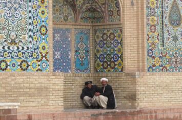 Zwei Männer sitzen vor einer bunten Moschee in Herat, Afghanistan