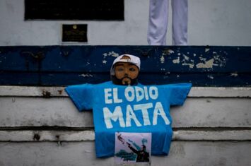 Ein blaues T-Shirt mit dem weißen Schriftzug "El Odio Mata - Hass tötet" liegt auf einer weißen Treppe. Darüber ist eine Maske von Präsident Bukele drapiert