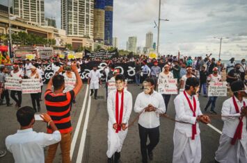 Protestierende mit Schildern, Bannern und Masken auf einer breiten Straße in Colombo, Sri Lanka