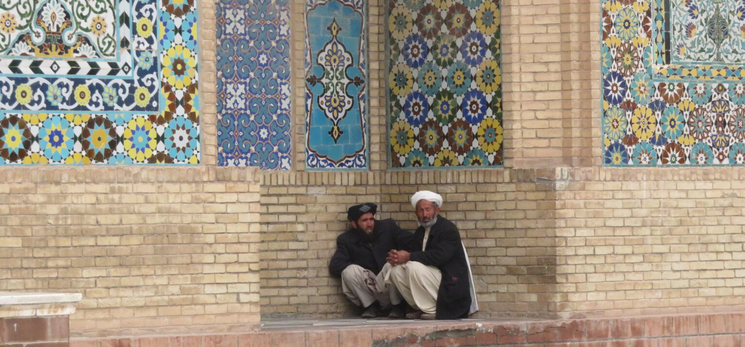 Zwei Männer sitzen vor einer bunten Moschee in Herat, Afghanistan