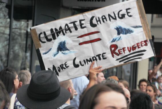 Protestschild mit Wellen und der Aufschrift »Climate Change mor Climate Refugees« in der Menge