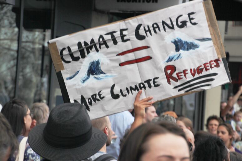 Protestschild mit Wellen und der Aufschrift »Climate Change mor Climate Refugees« in der Menge