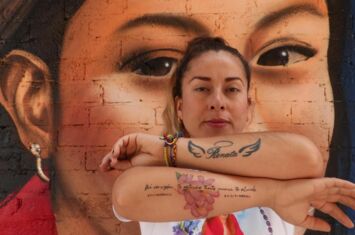 Portrait einer Frau mit Tatoos auf dem Arm und einem Murales im Hintergrund