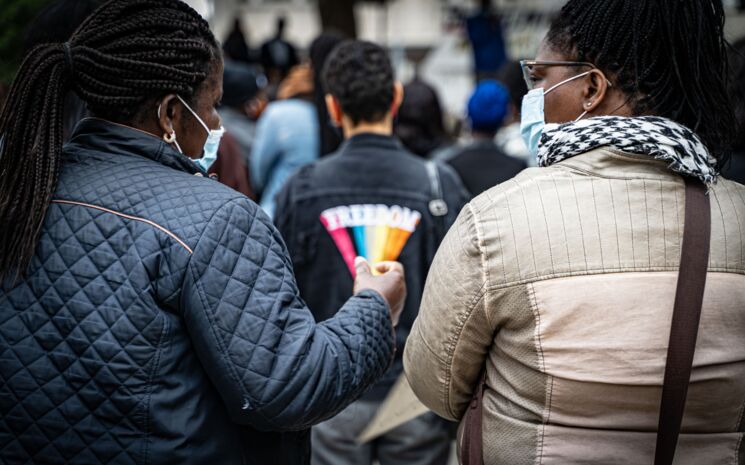 Bei der Mahnwache im Gedenken an George Floyd sind zwei Frauen von hinten seitlich zu sehen. Zwischen ihnen verschwommen im Vordergrund die Jacke einer anderen Person auf der steht Freedom. Freiburg, 06. Juni 2020 | Foto: Sévérine Kpoti