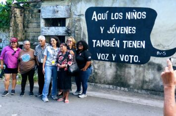 Eine Gruppe von Delegierten Caño Martin Peña CLT vor einem Wandbild mit der Aufschrift: »Hier haben auch Kinder und Jugendliche eine Stimme und ein Wahlrecht«