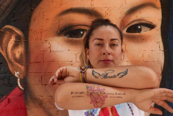 Portrait einer Frau mit Tatoos auf dem Arm und einem Murales im Hintergrund