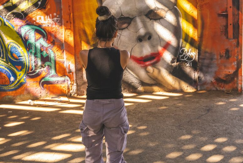 Person, die auf ein Graffit blickt: Eine Maske, die von einem Gesicht gezogen wird. Ist Identität gewählt oder aufgepresst?