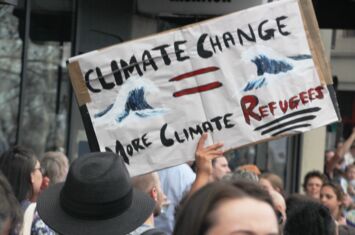 Protestschild mit Wellen und der Aufschrift »Climate Change mor Climate Refugees« in der Menge