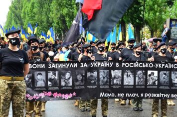 Viele Frauen demonstrieren in Uniform und mit ukrainischen Flaggen, sie halten ein schwarzes Banner, auf dem Fotos getöteter Soldatinnen zu sehen sind.