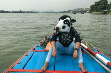 Person mit einer Maske einer heiligen Kuh auf einem Boot