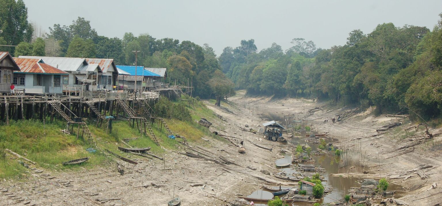 Häuser auf Stelzen und ein beinahe ausgetrockneter Fluss während der Trockenzeit in Indonesien
