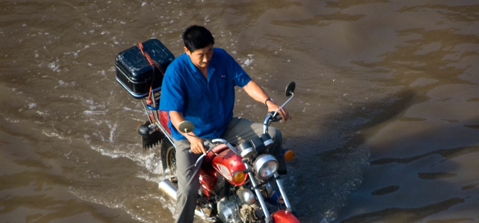 Mann fährt Motorrad durch eine überflutete Strasse in China. Die Rechte sieht Überschwemmungen im Ausland nicht als Problem.