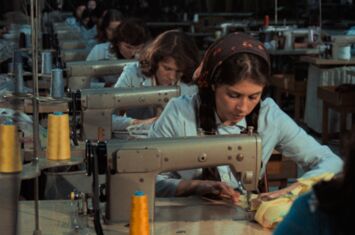 Filmstill aus »Kara Kafa«. Frauen in blauen Uniformen sitzen in einer Reihe über Nähmaschinen gebeugt.