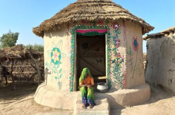 Eine Frau sitzt vor einem verzierten Lari Octa Green-Einraumhaus der Architektin Yasmeen Lari in Pakistan